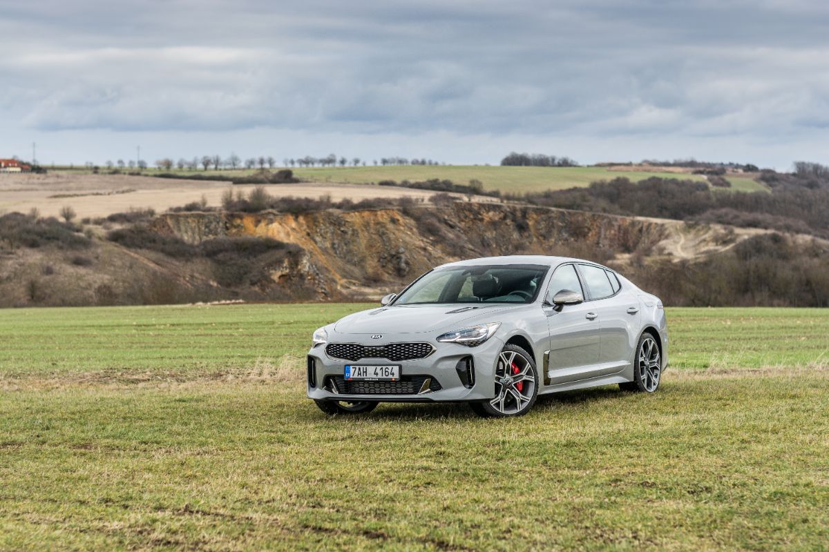 A photo shot of Kia Stinger car driving on the grass in nature background.