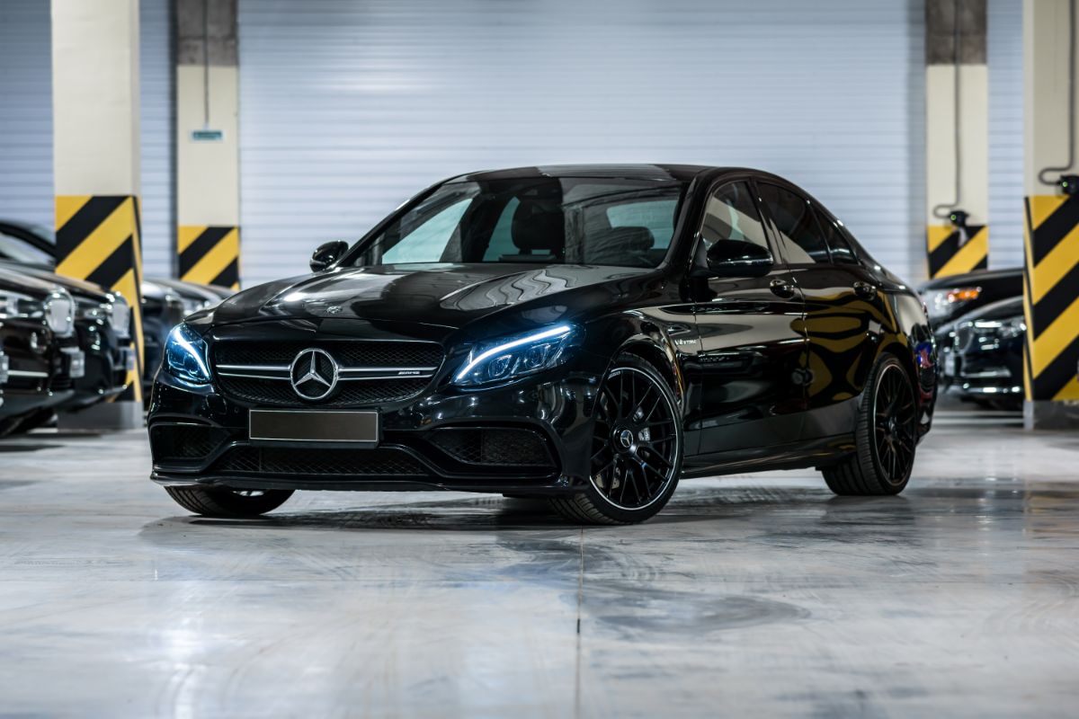 A black Mercedes-Benz C-Class AMG 63 with its headlights on in the front and from the side.