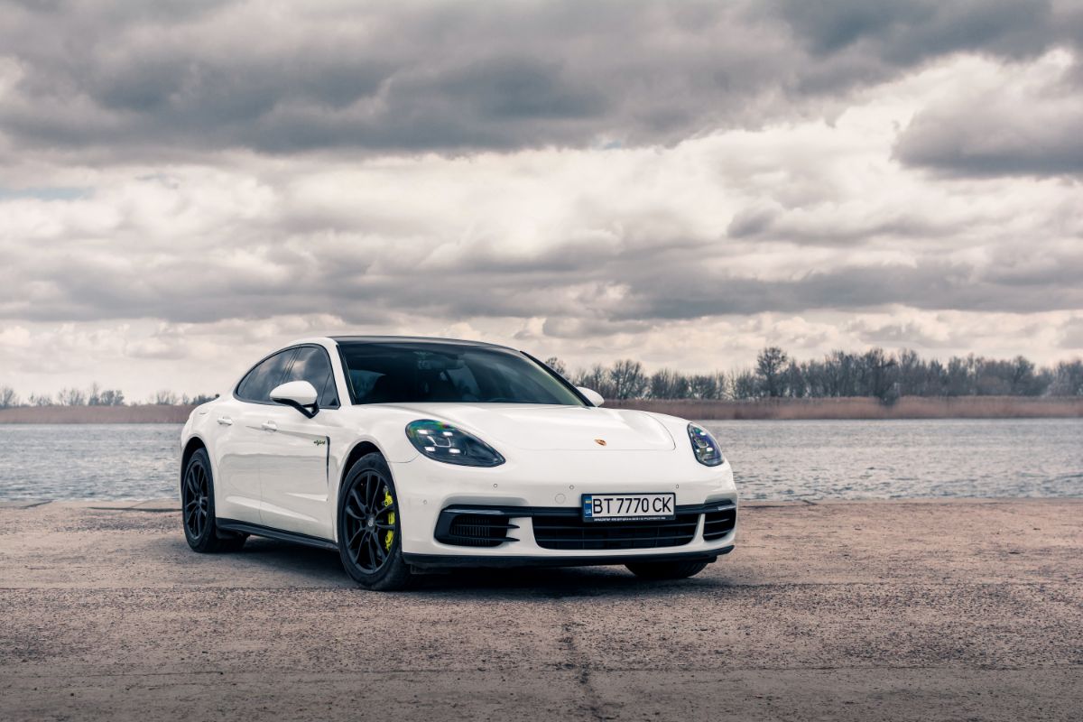 White colored Porsche Panamera against the river and cotton-like cloud background.