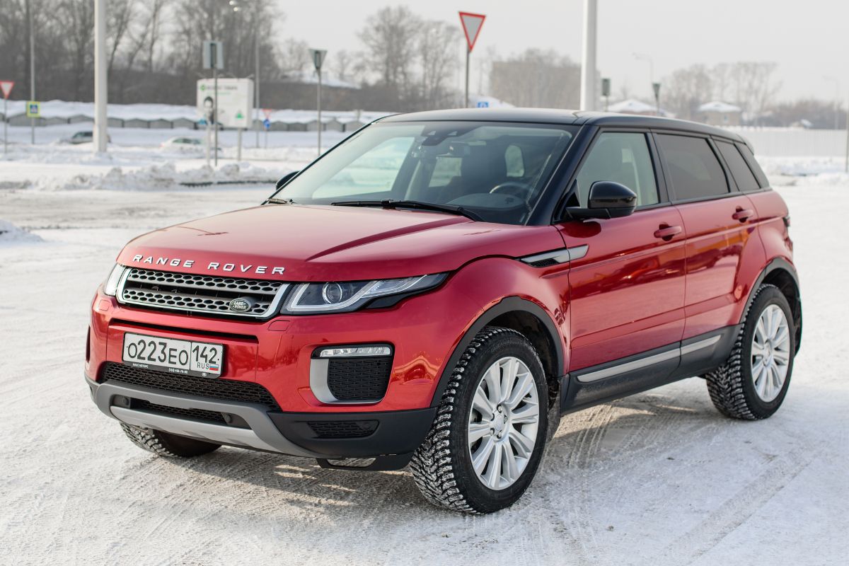 A red Range Rover Evoque car driving on the snow road during winter season.