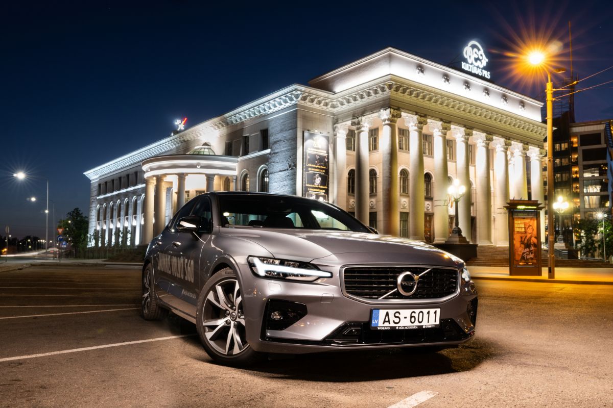 Shiny silver-colored Volvo S60 in parking slot in modern cityscape with light on.