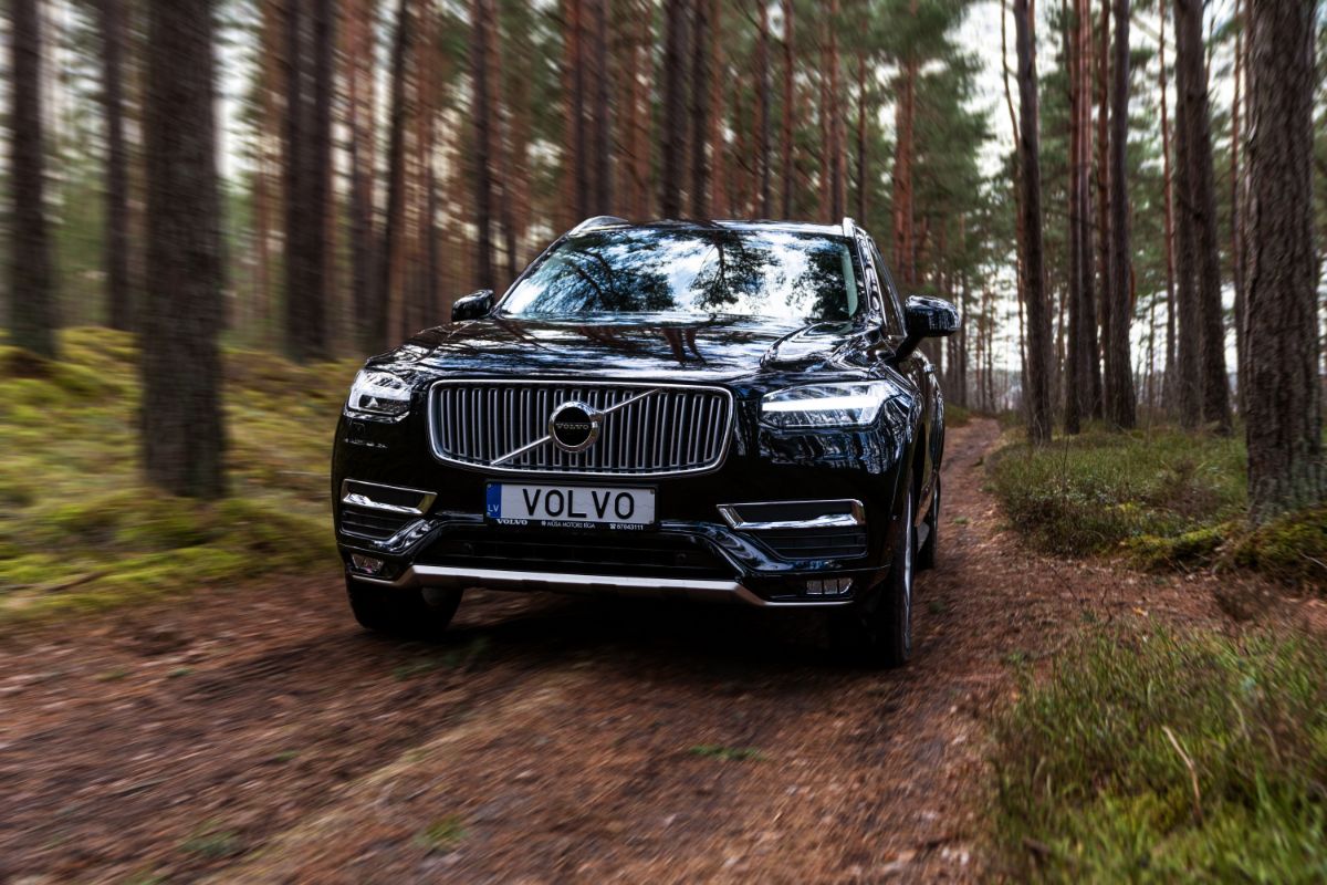 A mid-size luxury crossover SUV driving in forest motion blur with Volvo plate in front.