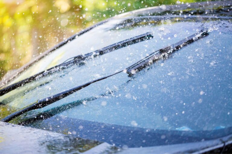 Car windshield with rain drops and frameless wiper blade close-up.