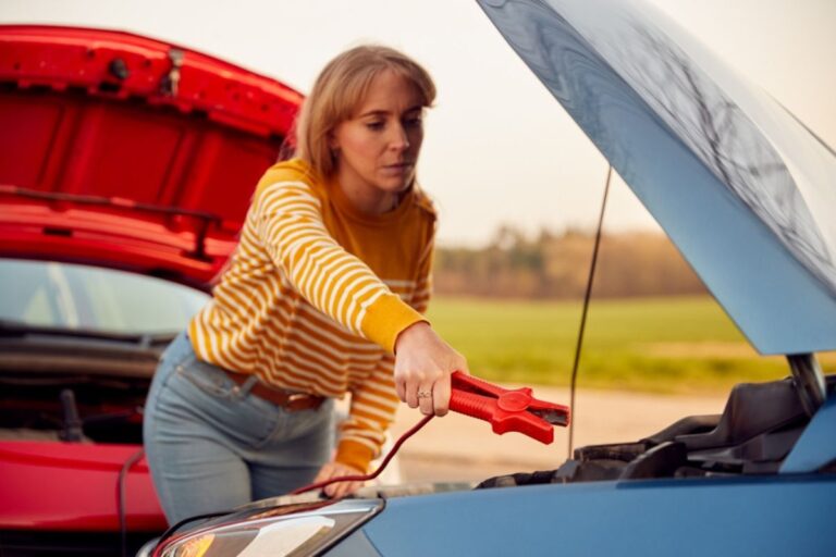 Woman attaching jumper cable to start car engine with flat battery.