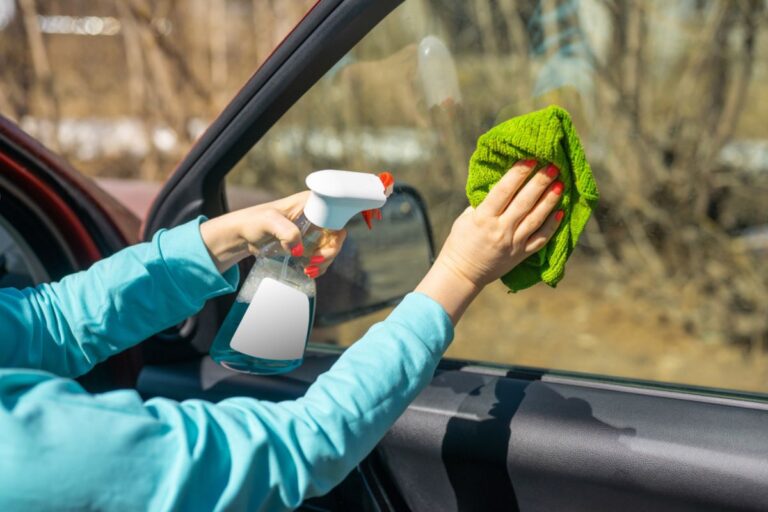 Female hands cleaning car window with green microfiber cloth and spray bottle with blank white label for your design.