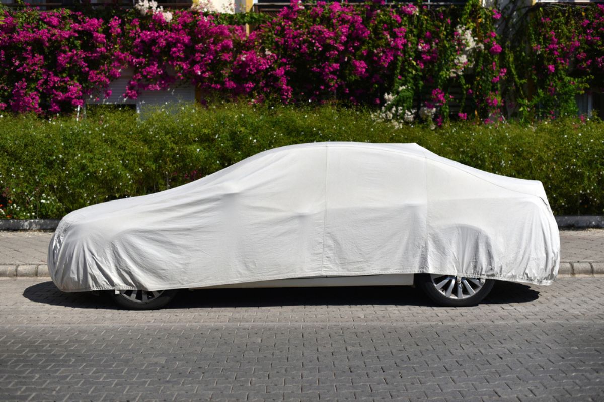 A parked car covered with a sun protection fabric on the street of green city.