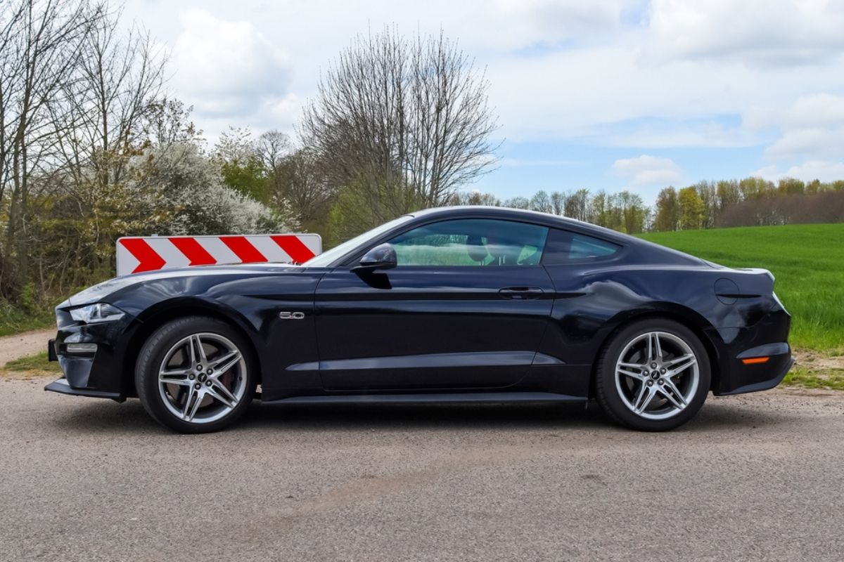 Side view on a black Ford Mustang model 2018 sports car parked on a sandy road.