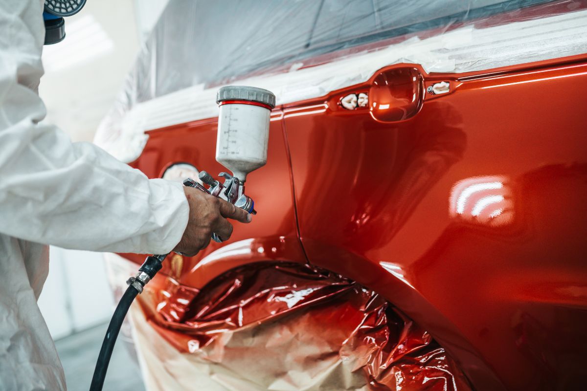 Man with protective clothes painting a car.