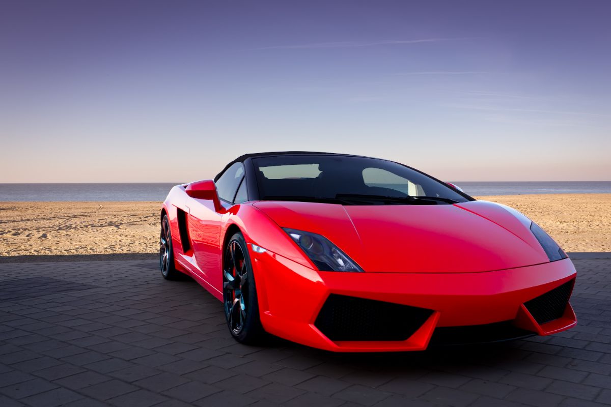 Front view of a red sports automobile at a beach at dusk.