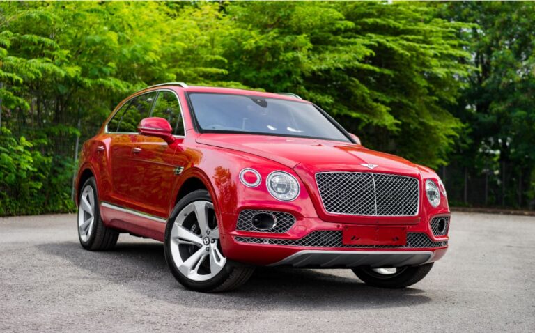 A photo of luxury red bentley bentyaga car with trees background.