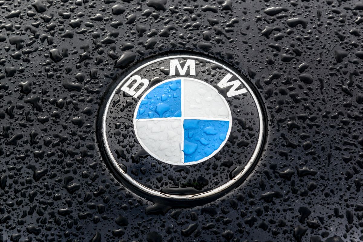 A zoom in photo of a rain wet BMW logo in a blac BMW luxury car.