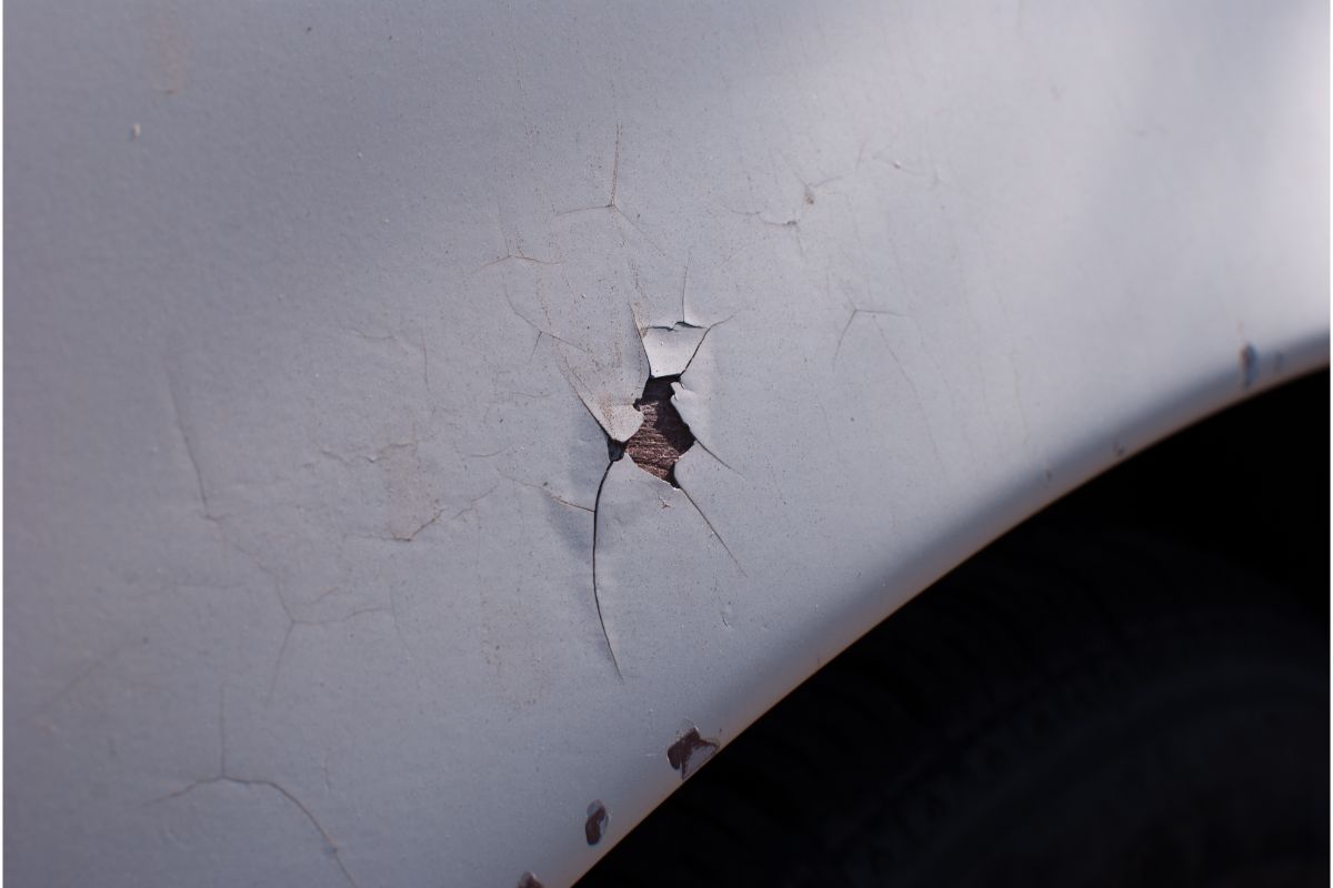 Close-up photo of a cracked paint on a white car fender.