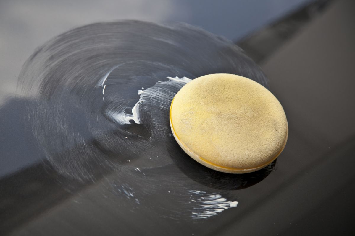 Zoom in photo of a sponge and a car wax on the surface of a car.