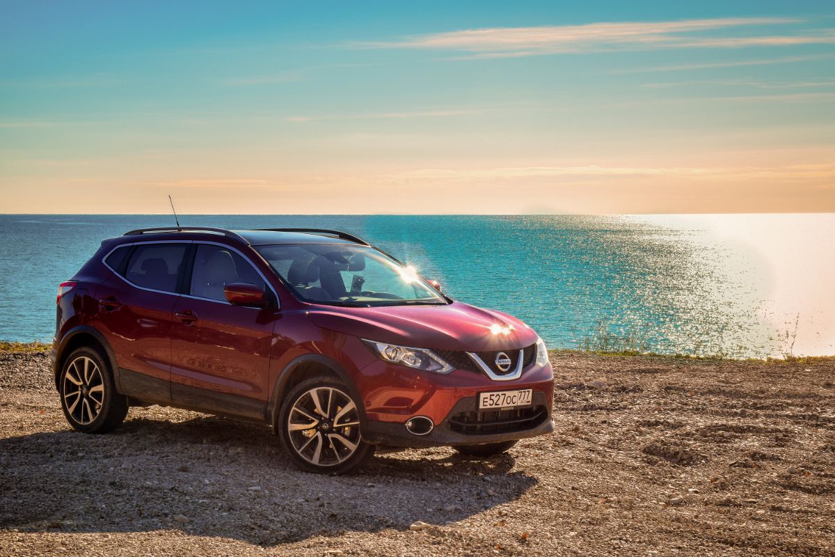 A picture of red crossove SUV easy driving near sea waters.