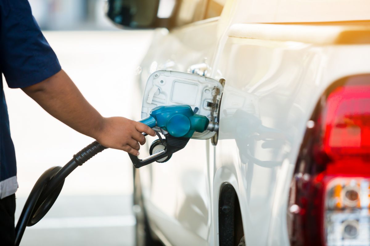 At the gas station, hand-filling the white pickup vehicle with gasoline, oil, and gas energy.