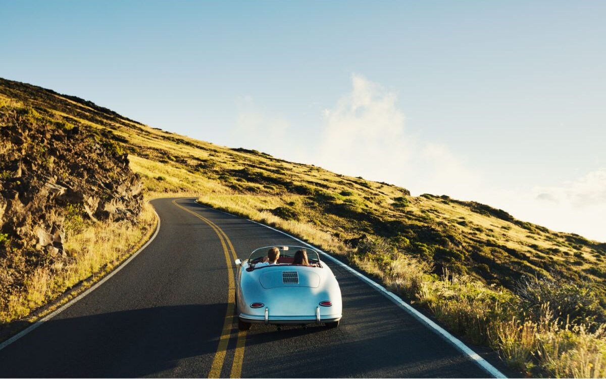 A couple in a vintage sports car traveling on a country road.