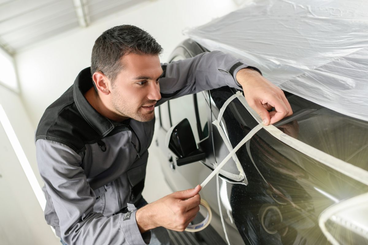 A car mechanic masking a car using a masking tape.