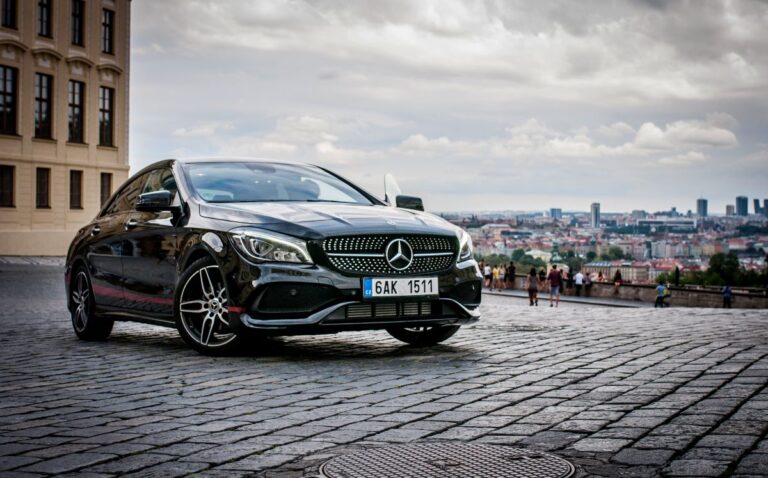 Front view of a shiny black Mercedes A-Class Sedan with a city background.