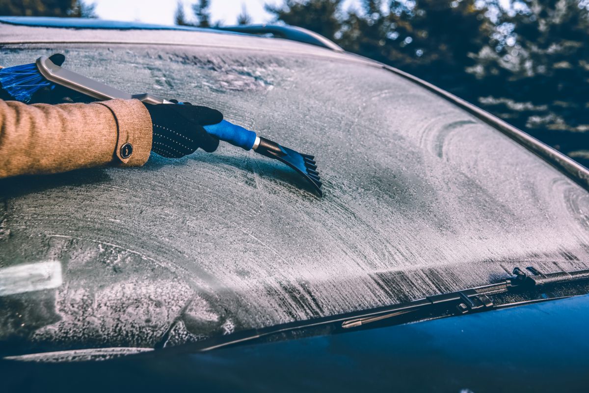 A man removing the snow from the frozen car window using a plastic scraper.