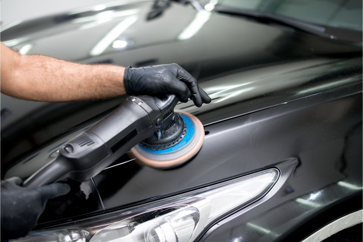 A man's hand wearing gloves while polishing a car using a polishing machine.