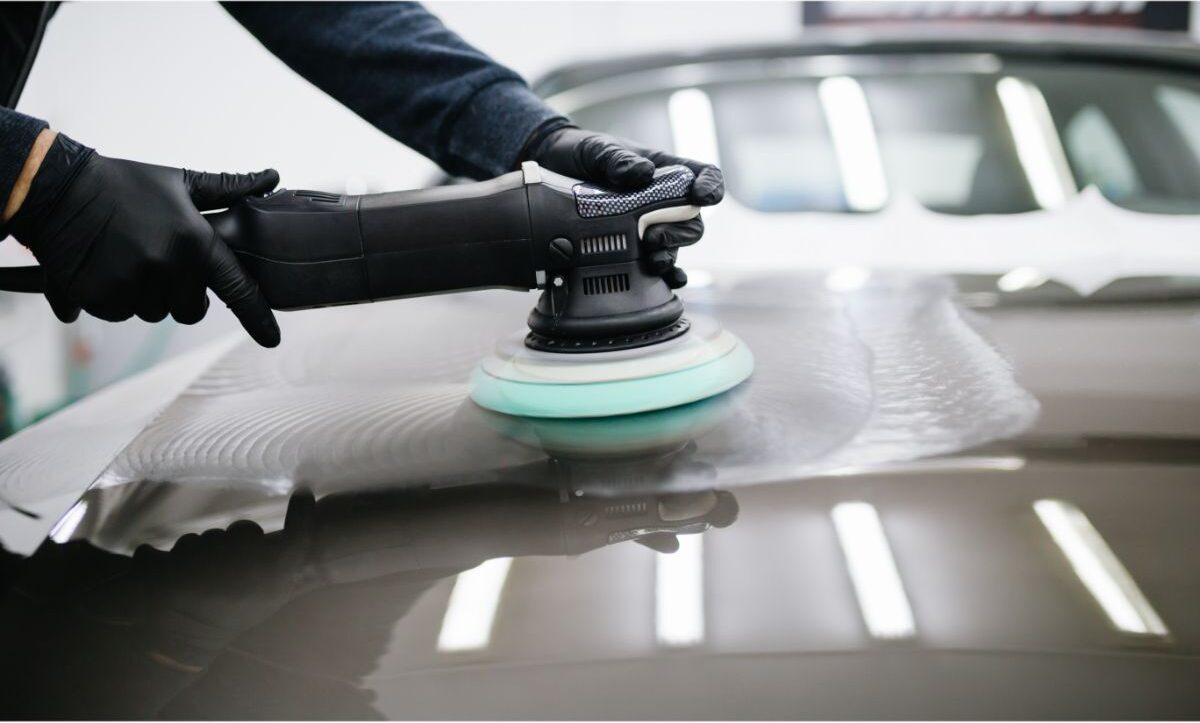 Man applying a car wax on his car while using a orbital polishing machine.