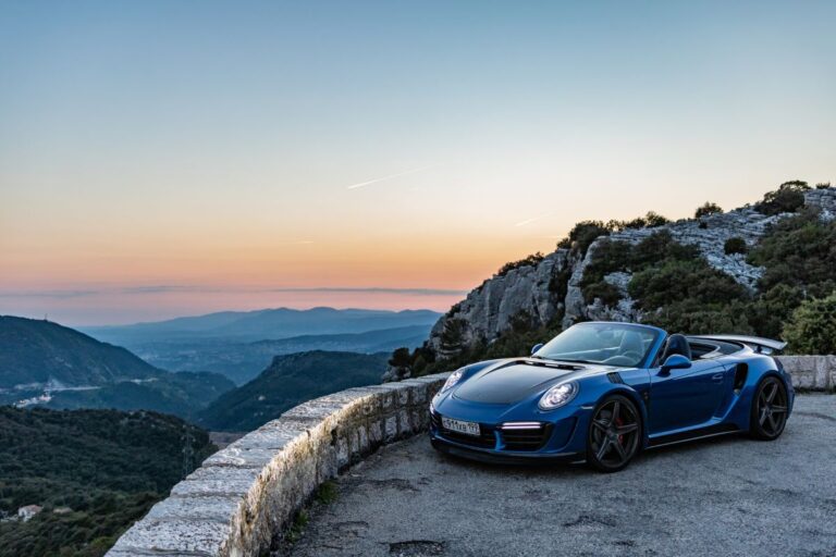 Blue Porsche 911 Cabriolet with an open roof and a mountain backdrop at dusk.