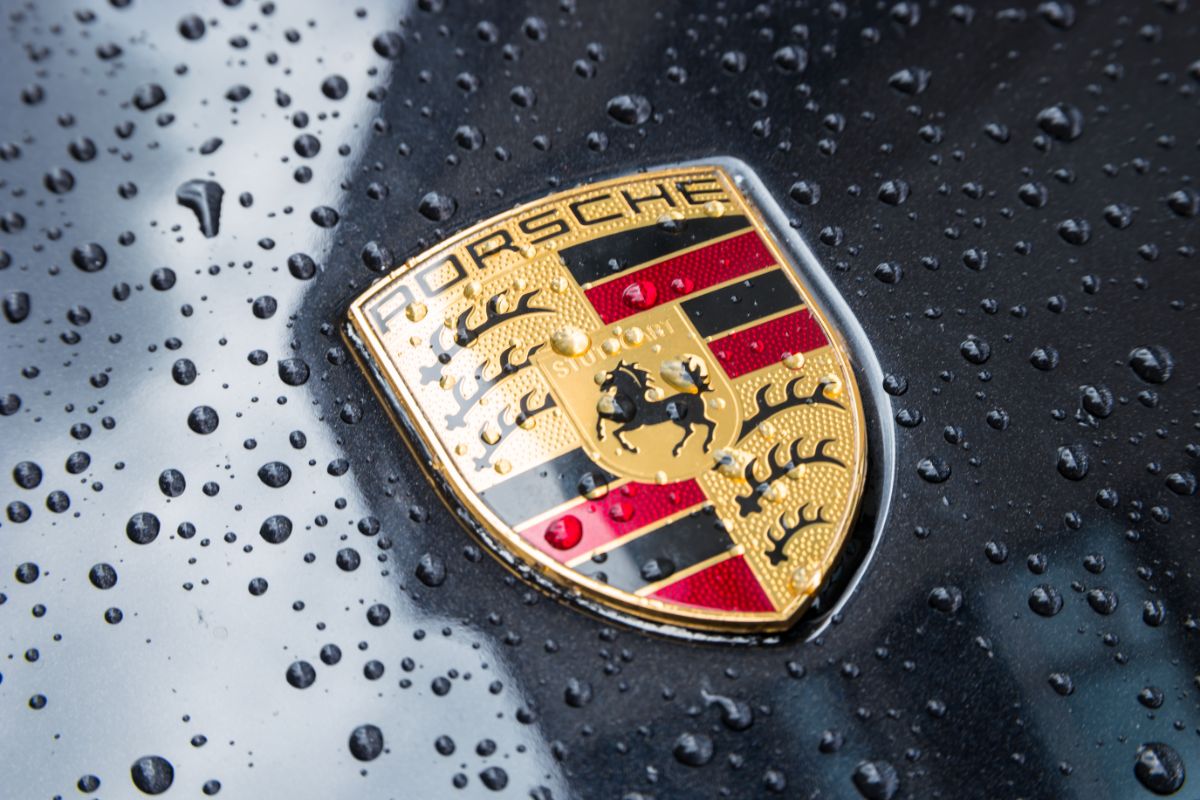 Zoom in photo of a wet Porsche logo in a black Porsche sportscar vehicle.