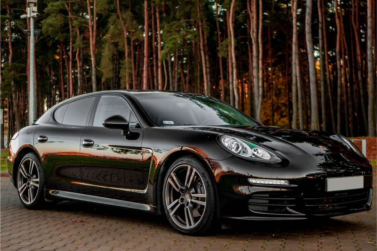 Front and side shot of black Porsche Panamera car driving on the road with trees at the back.