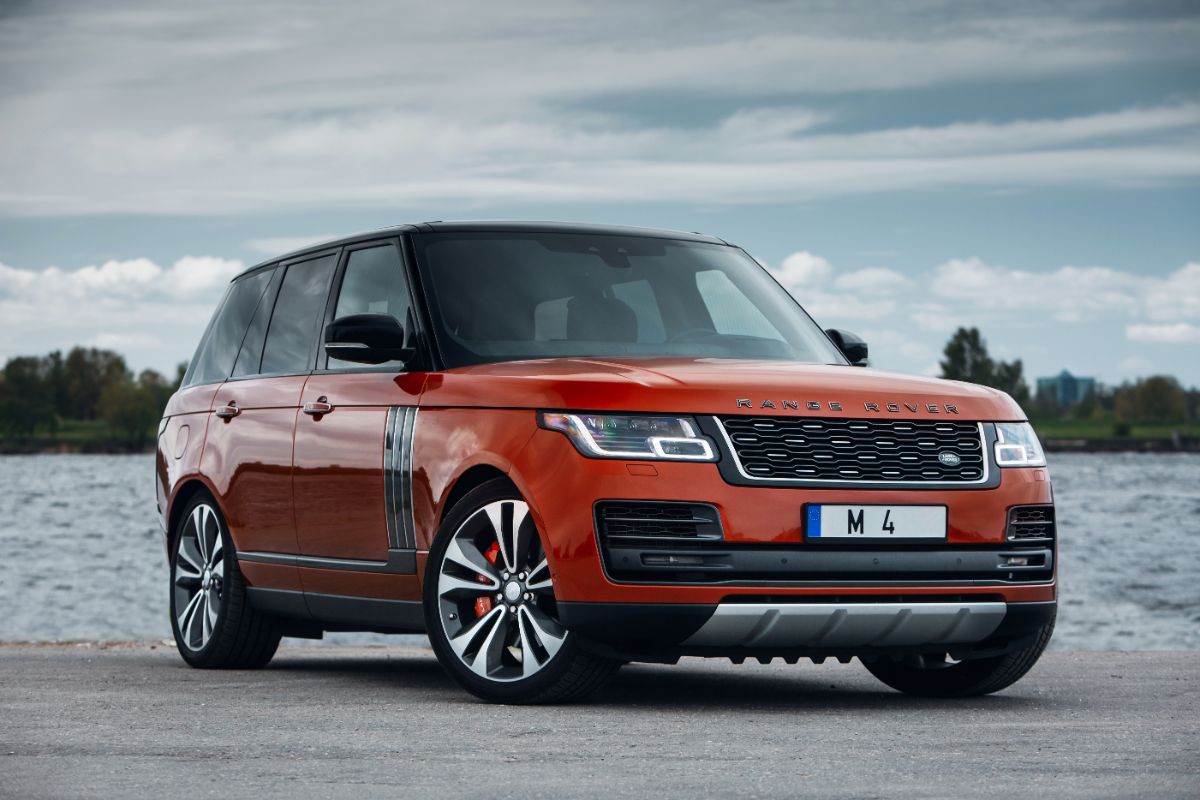 A luxurious Range Rover SV Autobiography red orange colorway parked near a river.