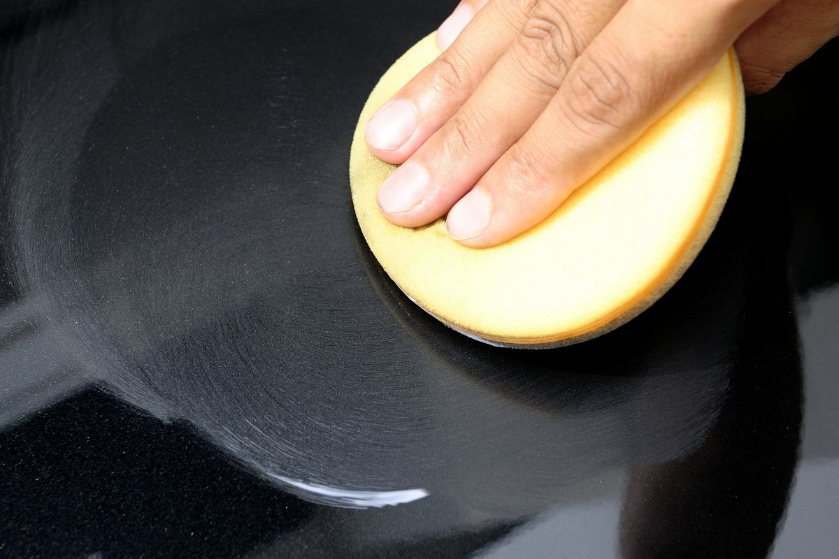 Close up photo of a man's hand holding a sponge while waxing the cars surface.