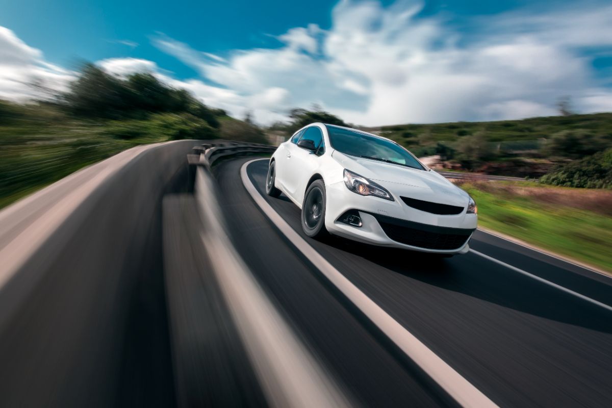 White automobile turning on a hilly road while moving quickly.