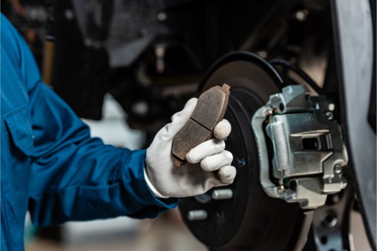 Cropped view of man's hand holding brake pad near assembled disc brakes.