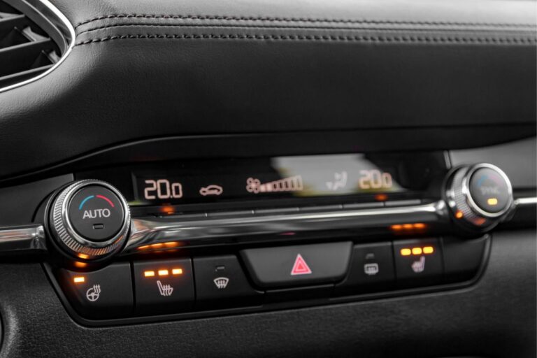 Close up shot of modern luxury car air conditioning control panel with steering wheel and seat heating options.