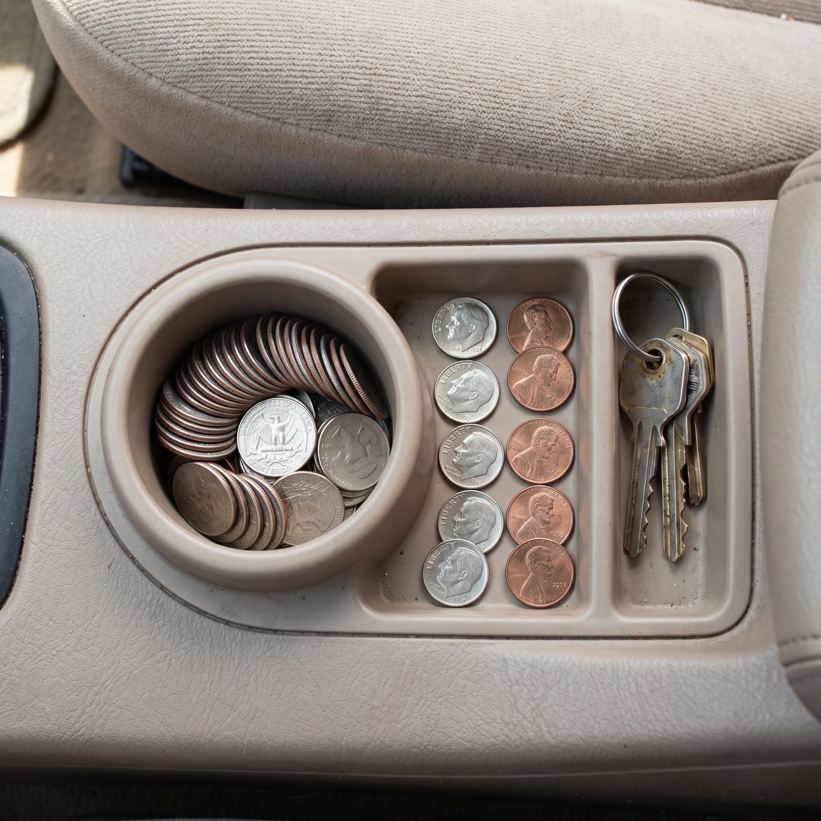 Built-in console coin cup filled with stacked quarters beside a small tray of dimes and pennies.