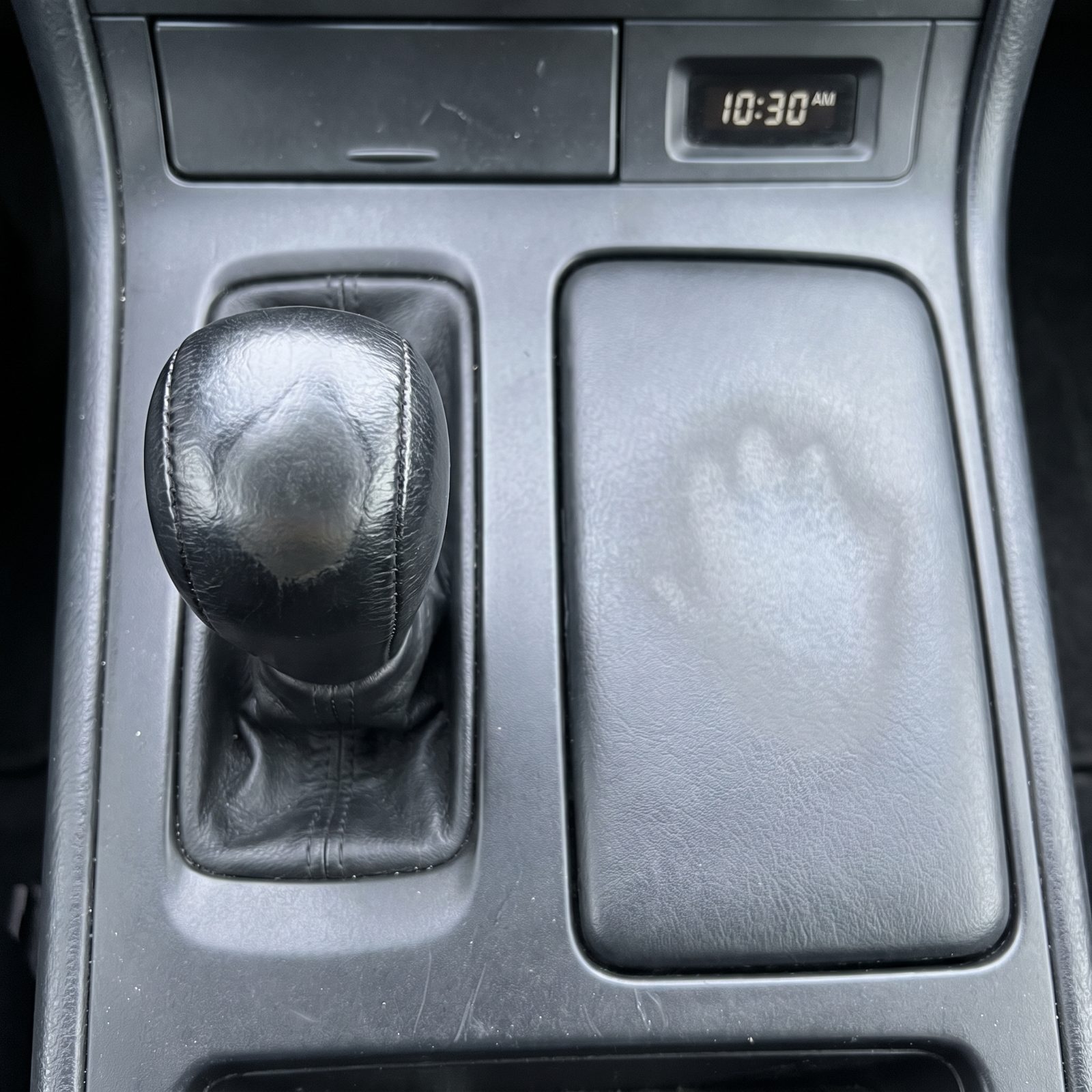Car gear shifter knob and console lid showing a polished worn patch where a hand repeatedly rests.