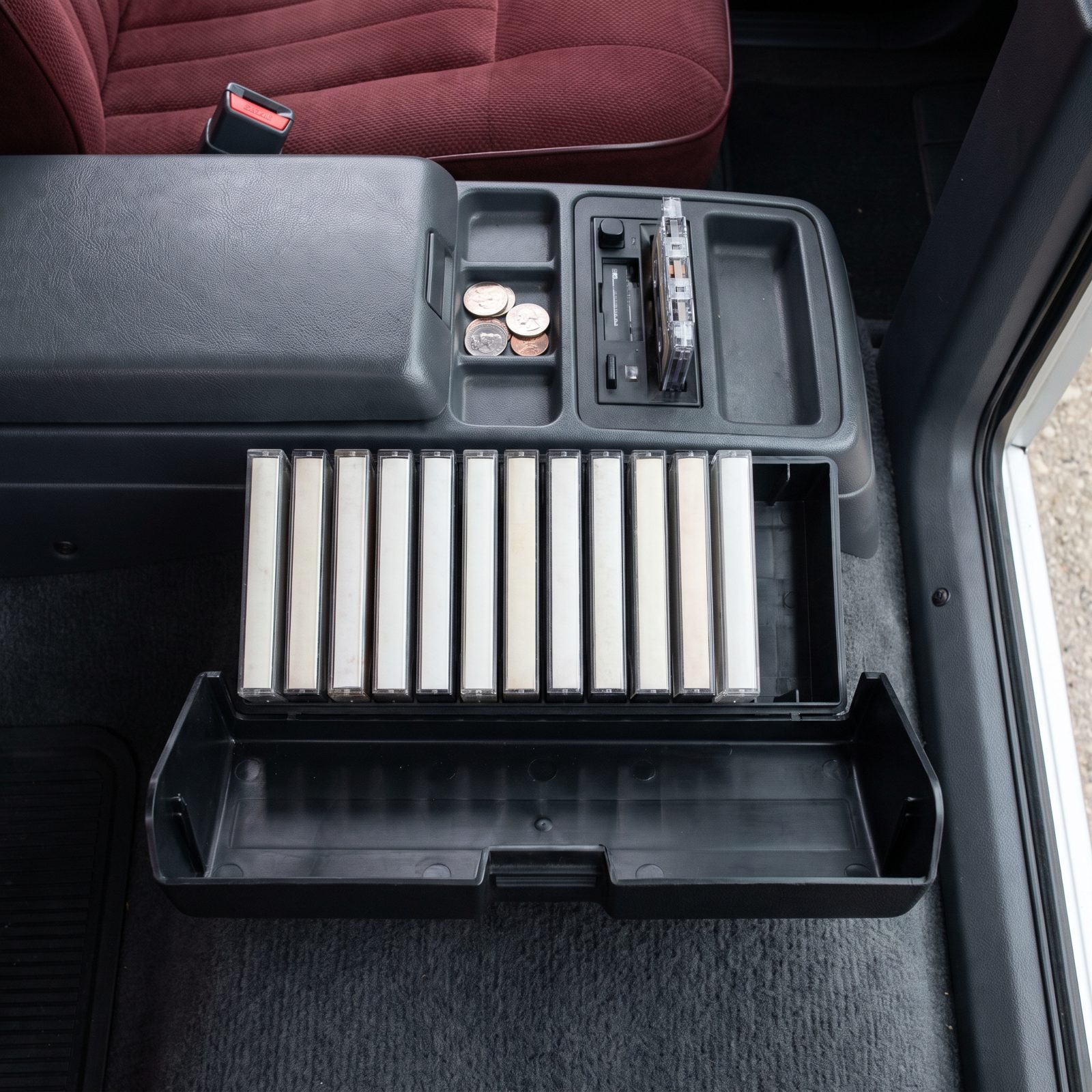 Open cassette caddy on a car console holding twelve tapes standing upright in a row.