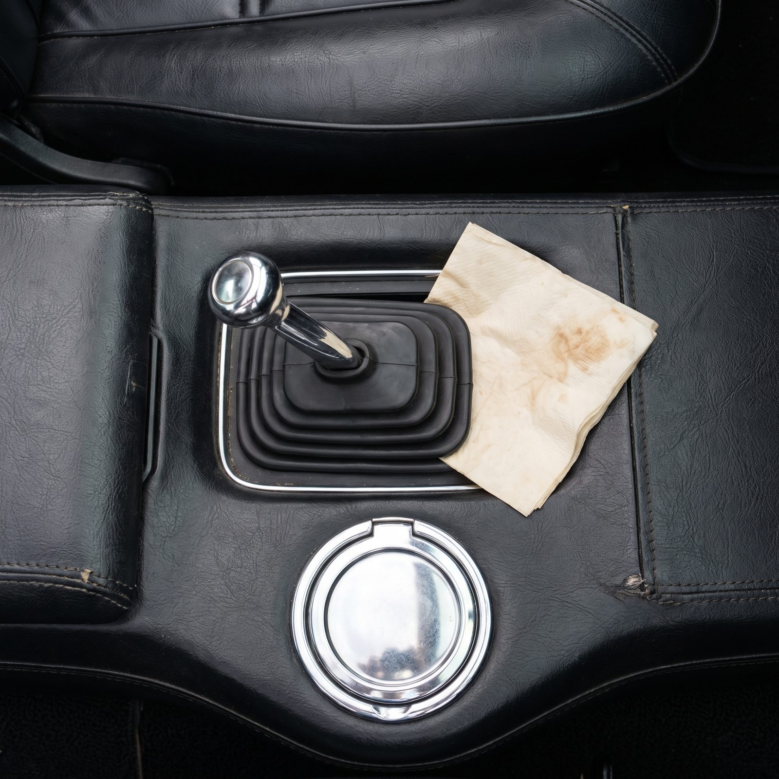Faded paper napkin tucked behind a chrome floor shifter in a vinyl console.