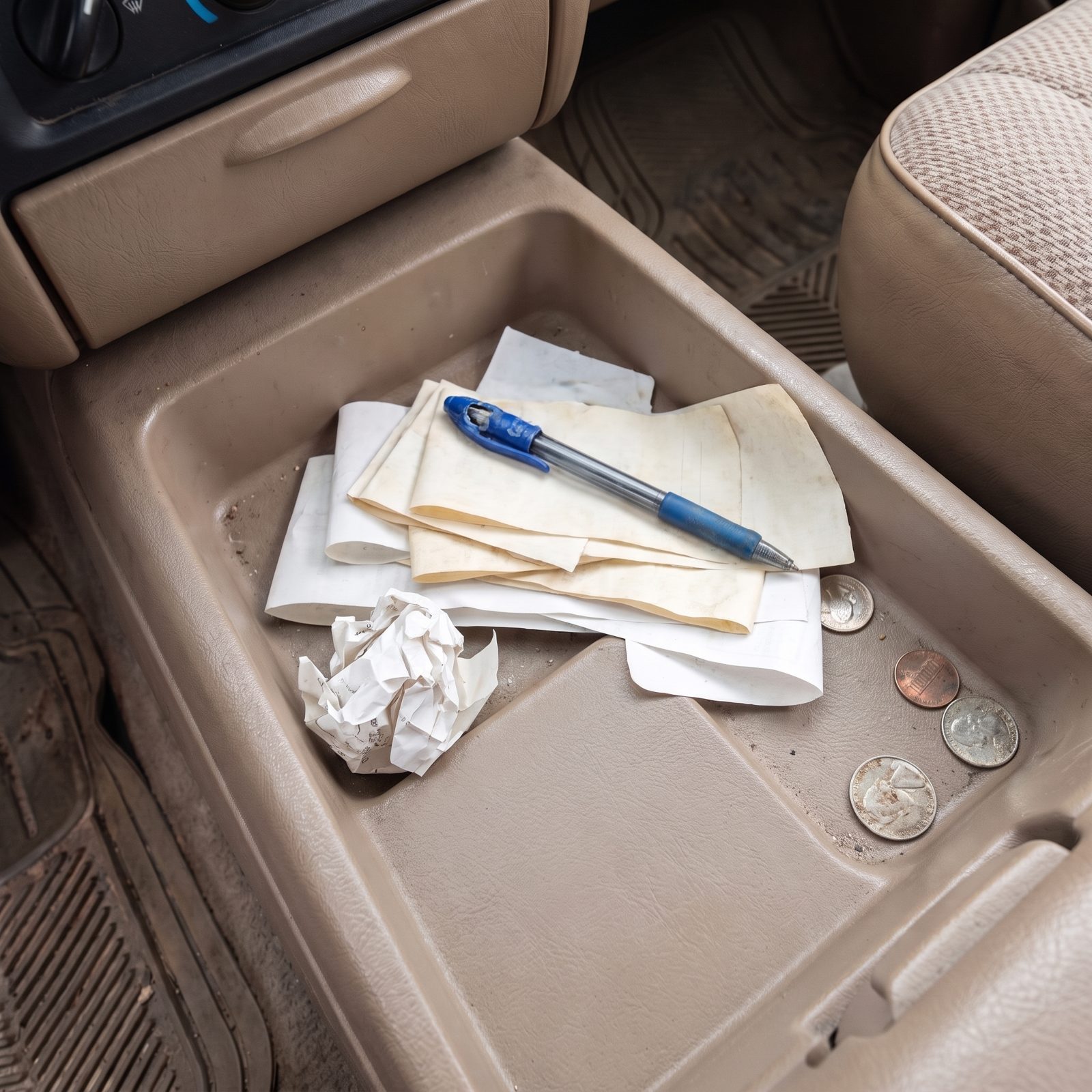 Console tray behind a truck shifter holding a stack of faded paper receipts and a pen.
