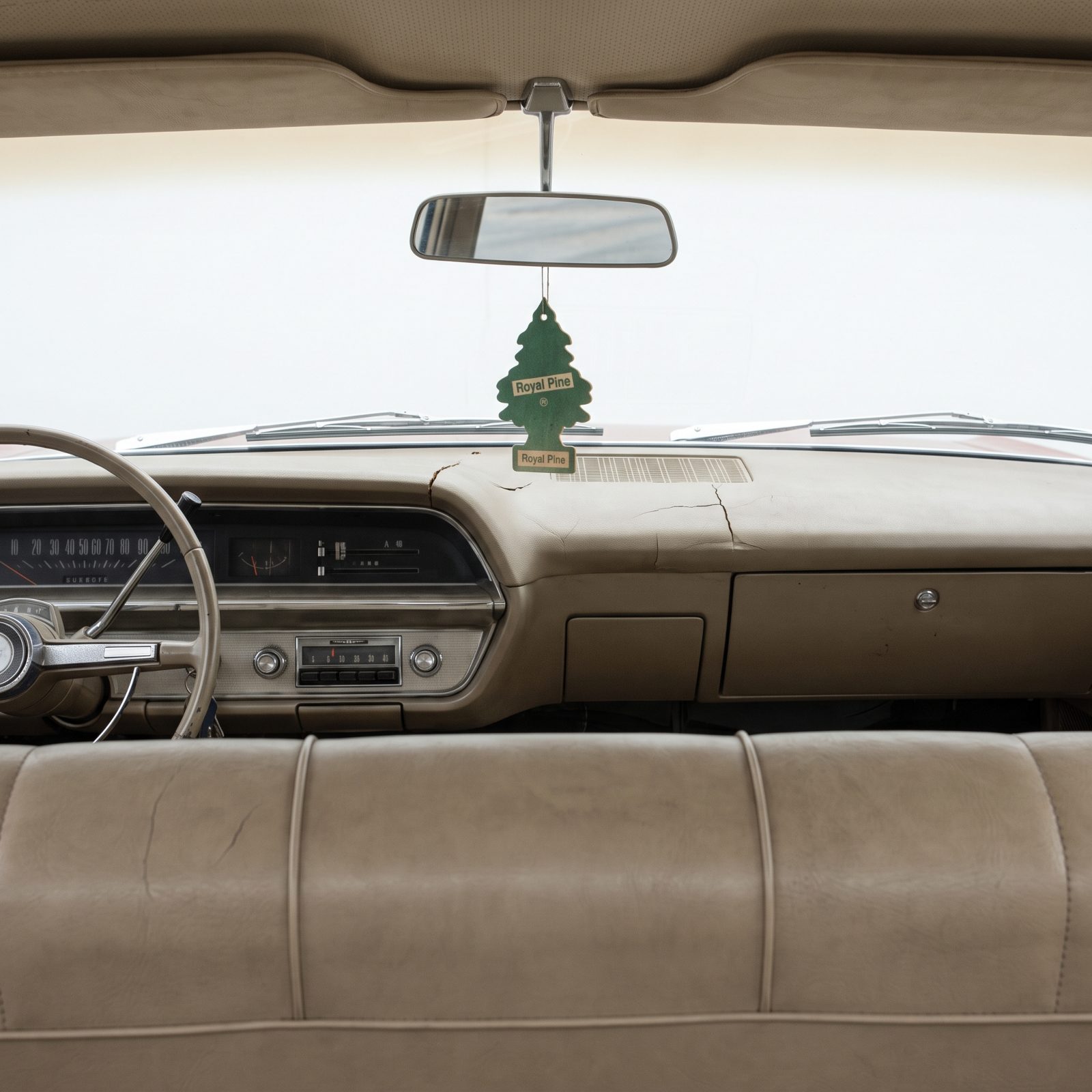 Interior of a 1960s car with the door open showing a cracked tan vinyl bench seat, a dashboard with round gauges, and an
